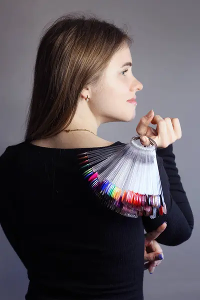 A blonde girl holds in her hand a palette with samples of nail polishes. Large selection of gel polish colors. Color display on the ring. Close-up photo