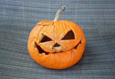 Ürkütücü bir ifadeye sahip buruşuk oyulmuş bir balkabağı desenli kumaş arka planda, Cadılar Bayramı çürümesini sembolize ediyor.