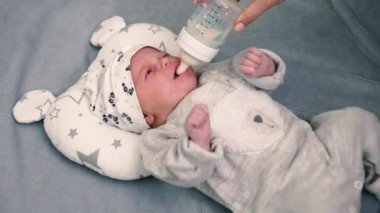 Küçük bebek bir odada duran bir şişeyle süt içer. Güzel kız yatakta uzanmış şişeden süt içiyor.