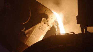 Patlama fırınındaki bir kepçeden sıvı erimiş metal dökülüyor. Parlak kıvılcımlar saçan sıvı çelik.