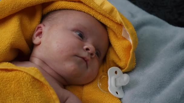 赤ちゃんは黄色のタオルの上に灰色の毛布に横たわっており 眠りに落ちるしようと美しい目で見えます — ストック動画