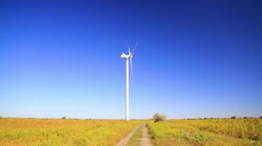 Mavi gökyüzüne karşı yeşil bir alanda rüzgar türbini enerji üretir. Yenilenebilir temiz enerji