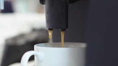 Siyah kokulu espresso beyaz bir kaba dökülür. Fasulyeli otomatik kahve makinesi bir espresso içeceği dolduruyor.