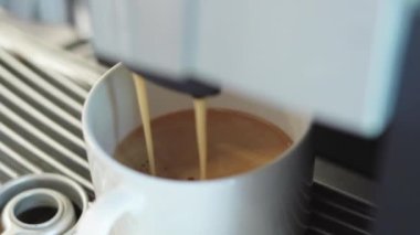 Kahve makinesi sabahları espresso ve ristretto yapıyor. Sabahları sıcak, aromatik kahve. Siyah espresso beyaz bardağa doluyor.