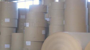 Large spools of brown paper stand in kraft paperboard and box production warehouse