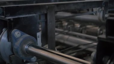 Conveyor mechanism, gears and bearings in motion close-up. Metal shaft spins on paper production