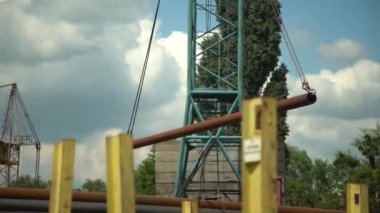 Gantry Turnası, açık hava deposundaki çelik fabrikasında büyük boruları taşıyor. Fabrikada metal ürünleri üretiliyor.
