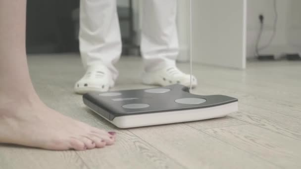 女性は自分自身を計量 重量損失と食事療法 医者の監督の下で診療所の規模の足の閉鎖 — ストック動画