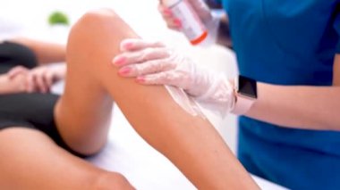 Kozmetik uzmanı, tüy dökülmesi için kızın bacağına ultrason lazer aldırma jeli uyguluyor.