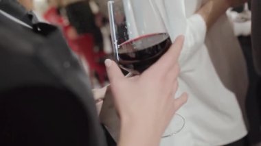 Kurumsal bir akşam partisinde bir kızın elinde bir kadeh kırmızı şarap.