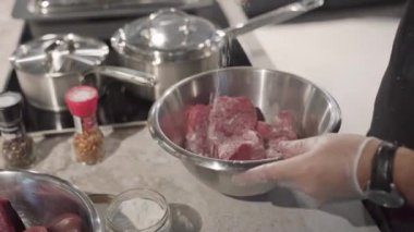 Aşçı eti bir kasede marine eder. Şefin eldivenli elleri salamurayı karıştırıyor. Bir restoranda profesyonel mutfak.