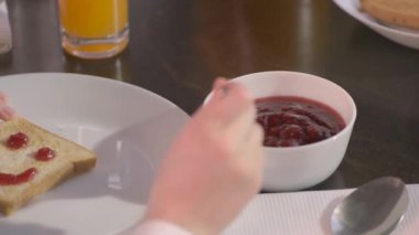 child spreads jam or jam on a toasted piece of bread at breakfast. A close-up hand draws a smile with the jam