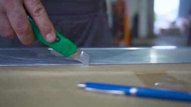 Metal cetvel boyunca kağıt kesmek için bıçak kullanan bir işçinin yakın çekimi. Görüntü, bir zanaat veya atölye ortamında yapılan ayrıntılı ve titiz çalışmaları gösteriyor