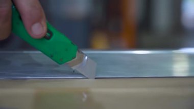 Metal cetvel boyunca kullanışlı bir bıçakla kağıt şablonu kesen bir işçinin yakın çekimi. Bu araç bir çalışma alanı ayarında hassas ve doğru kesme için kullanılır.