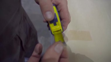 Elinde mezurası olan bir işçi, onu çalışma masasının üzerinden söker. Bir inşaat işçisi doğru bir yakın çekim ölçümü alır