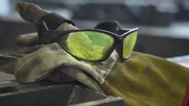 Sarı güvenlik gözlükleri ve eldivenler bir metal dükkanında tezgahta duruyordu. Sanayi güvenliğinin, işçiliğin ve bir fabrika veya üretim tesisinde çalışma ortamının sembolik imajı