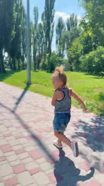 Yaz kıyafetleri içinde mutlu küçük kız park yolunda koşuyor, güneşli havanın ve özgürlüğün tadını çıkarıyor.