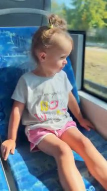 Küçük kız tramvayda gezmekten hoşlanıyor, pencereden merakla bakıyor. Neşe atmosferi, çocukluk ve kentsel hareket