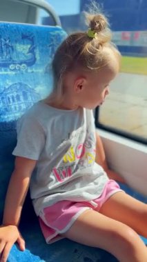 Küçük kız mutlu bir şekilde tramvaya biniyor ve merakla pencereden dışarı bakıyor. Seyahat ve keşif atmosferi