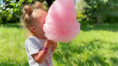 Küçük kız dışarıda pembe pamuk şekerin tadını çıkarıyor. Neşe, eğlence ve yaz tatili dolu bir atmosfer.