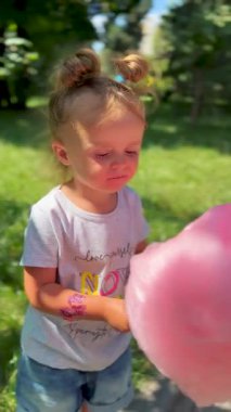 Küçük kız dışarıda yürürken pamuk şekerin tadını çıkarıyor. Çocukluğun, neşenin ve tatlı ikramların sembolü.