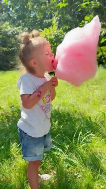 Küçük kız mutlu bir şekilde parkta pamuk şeker yiyor. Neşenin, çocukluğun ve aile gezintilerinin sembolü.