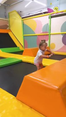 Oyun merkezinde trambolinde zıplayan küçük bir kız. Sağlık, koordinasyon gelişimi ve çocukların fiziksel aktivitesi kavramı