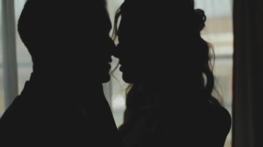 Birbirine aşık bir kadın ve erkeğin silueti pencerede öpüşmeleri, şefkat. Yeni evli çiftin siluetini orta boy vurdu. Evlilik, romantik bir ortam. Yüksek kaliteli FullHD görüntüler