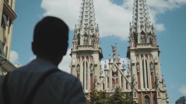 Back view of the hipster guy looking out while standing near Roman Catholic Church background. High quality 4k footage
