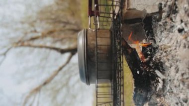 Nehir kenarındaki kamp ateşinde yemek pişirmek. Bir yürüyüşçü sosisli yumurta kızartır. Küçük bir tencere derme çatma bir ocağın üzerinde duruyor. Yüksek kalite 4k görüntü