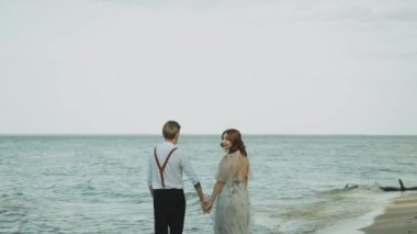 Güzel, genç ve aşık bir çift sahilde yürürken dalgalar sahili kasıp kavuruyor. Birbirine aşık bir çift el ele tutuşuyor. Yüksek kalite 4k görüntü