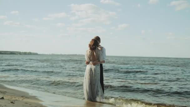 一对年轻貌美的恋人在沙滩上散步 海浪冲刷着海滩 享受着散步的乐趣 恋爱中的夫妻手牵手 高质量的4K镜头 — 图库视频影像