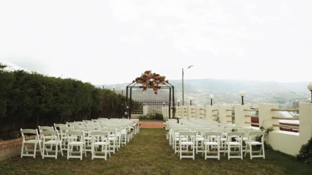 結婚式のアーチと白い木製の椅子が山の端に立っている Booスタイルの結婚式の装飾 背景に雲や山 スローモーション 高品質のフルHd映像 — ストック動画