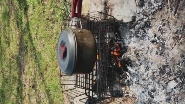 Nehir kenarındaki kamp ateşinde yemek pişirmek. Bir yürüyüşçü sosisli yumurta kızartır. Küçük bir tencere derme çatma bir ocağın üzerinde duruyor. Yüksek kalite 4k görüntü