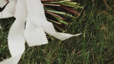 Gelinin düğün aksesuarları, bukette yakın plan kurdeleler, düğün buketi. Gelinin sabahı. Yeşil çimenlikteki düğün aksesuarları. Yüksek kaliteli FullHD görüntüler