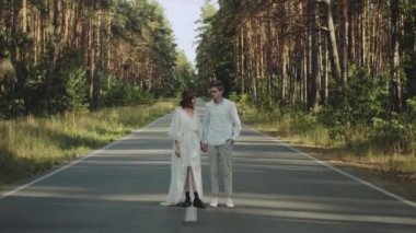 Aşık hippi çift güzel bir yerde yürür, el ele tutuşur, kadın ve erkek, boş yolda pikoresk çam ormanlarında sarılır ve eğlenir. Yüksek kalite 4K görüntü. yavaş çekim