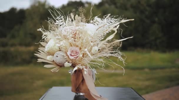 新娘的一束干花矗立在一个花瓶的后面 外面是绿树 花束上的彩带在婚礼当天的风中形成 动作缓慢 4K镜头 — 图库视频影像