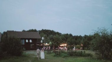 Gelin ve damadın düğün partisine yürüyüşünün arka görüntüsü. Boho tarzı elbiseli gelin. Gün batımında sevgili bir çift. Yüksek kalite 4k görüntü