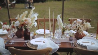 Kapalı masa, mum ve kurutulmuş pastel çiçeklerle servis edilir. Boho tarzı düğün yemeği, tabaklar ve bardaklar için. Kimse vurulmayacak, yavaş çekim yapılacak. Yüksek kalite 4k görüntü