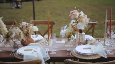 Kapalı masa, mum ve kurutulmuş pastel çiçeklerle servis edilir. Boho tarzı düğün yemeği, tabaklar ve bardaklar için. Kimse vurulmayacak, yavaş çekim yapılacak. Yüksek kalite 4k görüntü