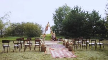 Açık hava düğün töreninde çok güzel bir bohem kemeri süsü. Pastel renklerden, kurumuş çiçeklerden, tahta sandalyelerden ve eski moda halılardan oluşan çiçek kompozisyonları. Yaz düğünü. Yüksek kalite 4k