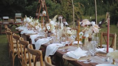 Orta boy servis edilen ve mumlarla süslenmiş, kurutulmuş ve pastel çiçeklerle boho tarzı düğün yemeği, tabaklar ve bardaklarla süslenmiş, vurulan kimse yok, ağır çekim. Yüksek kalite 4k görüntü