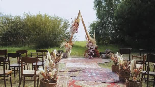 屋外の結婚式で美しいボヘミアンアーチの装飾 パステルカラー ドライフラワー 木製の椅子や昔ながらのカーペットの花の組成物 夏の結婚式 高品質4K — ストック動画