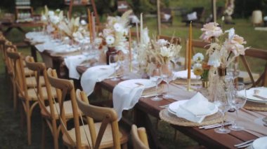 Boho tarzı düğün yemeği, tabak ve şarap bardakları için mum ve kurutulmuş pastel çiçeklerle servis edilmiş ve dekore edilmiş bir masa. Yüksek kalite 4k görüntü