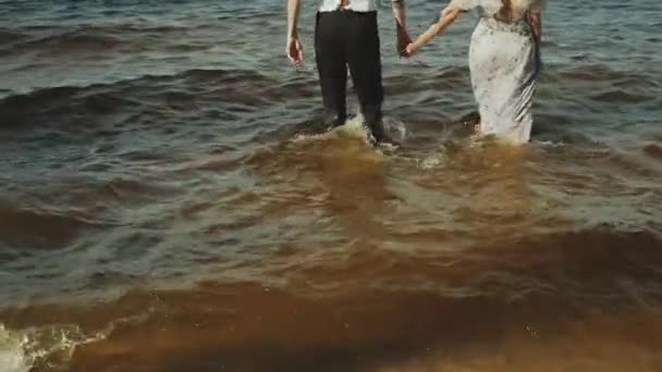 一对年轻貌美的恋人在沙滩上散步 海浪冲刷着海滩 享受着散步的乐趣 恋爱中的夫妻手牵手 高质量的4K镜头 — 图库视频影像