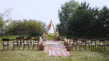 Açık hava düğün töreninde güzel bir kemer süslemesi. Pastel renklerden, kurumuş çiçeklerden, ahşap sandalyelerden ve eski moda halılardan oluşan çiçek kompozisyonları. Yaz düğünü. Yüksek kalite 4k görüntü