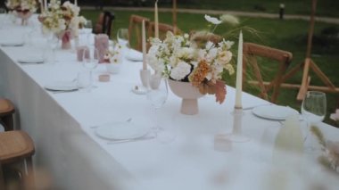 Pastel çiçekler, mumlar, eski moda sandalyeler ve küçük düğün partisinde arka planda eski moda lambalar olan yakın plan düğün masası ayarı, yavaş çekim. Yüksek kalite 4k görüntü