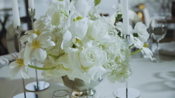 結婚式での華やかな装飾 レストランのテーブルには白い花のクローズアップ花束が置かれています バラやキャンドルと花の美しい配置 スローモーション 高品質4K — ストック動画