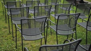 Back view of black empty chairs at the wedding ceremony in a park, close-up, green lawn on the background, slow motion. High quality 4k footage