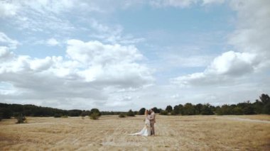 Loving bride and groom embrace together facing each other, beautiful couple in the countryside, Bride in boho dress and groom in suit standing across the field, slow motion. High quality 4k footage